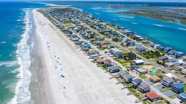 An aerial view of a coastal resort with rows of beachside villas, a sandy beach, and clear blue waters. - Mountains to Sea by Topsail Realty (Holly Ridge)