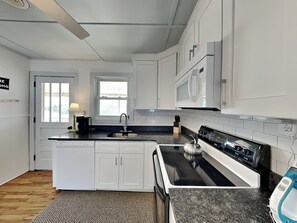 A modern kitchen with white cabinetry, a black countertop, a stainless steel sink, a stove, and a microwave.