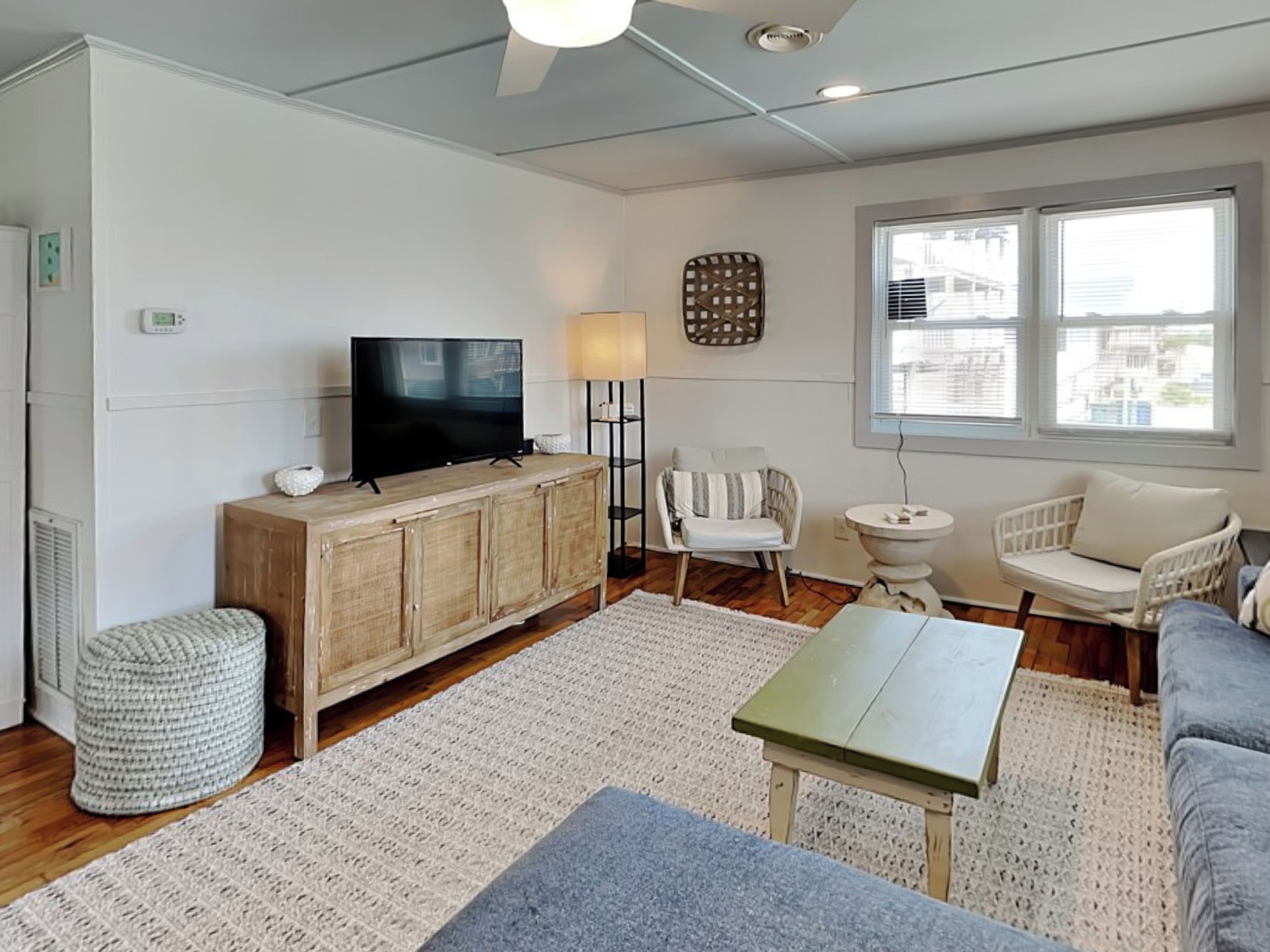 A living room with a wooden cabinet, a television, a lamp, two chairs, a small table, and a large window.