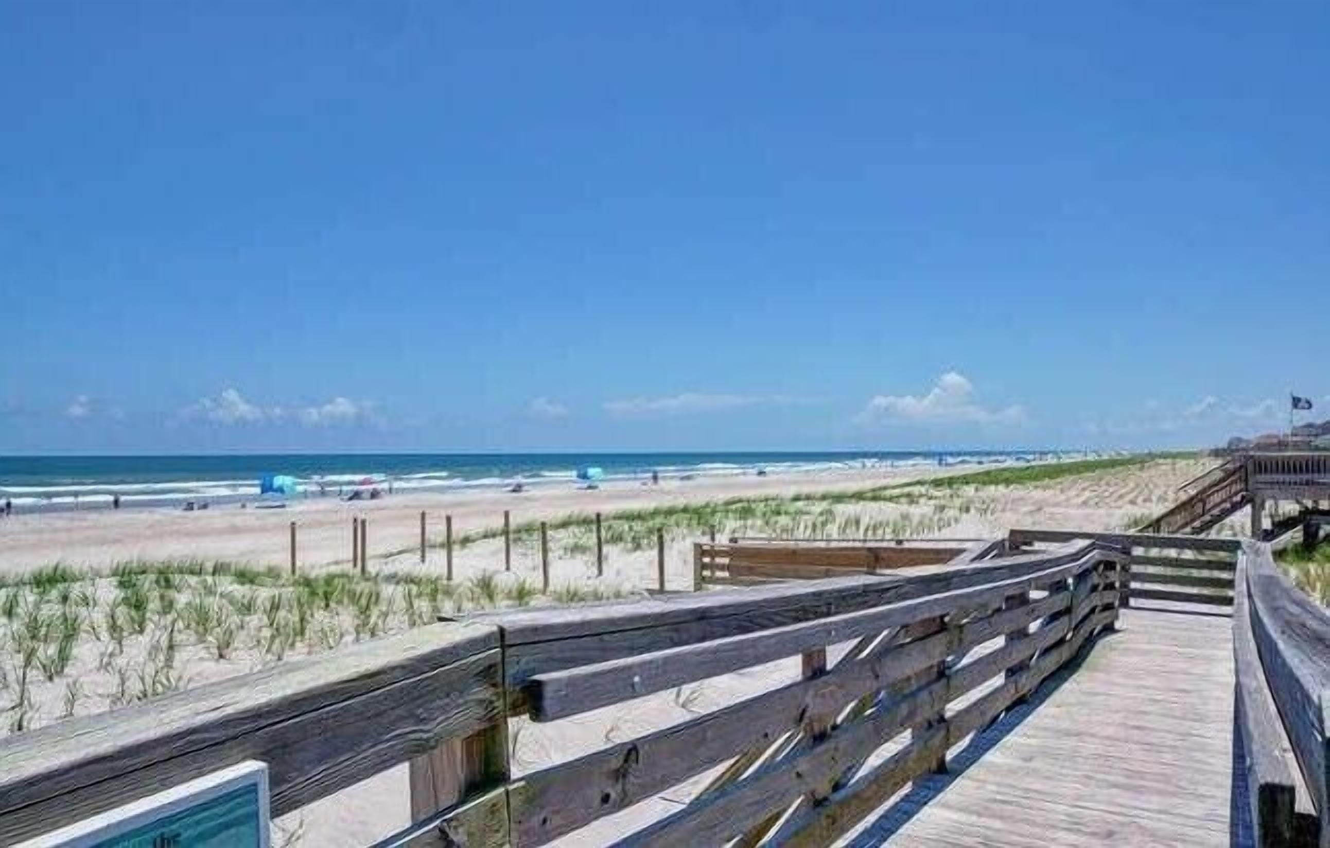 A wooden boardwalk leading to a beach with a clear sky.