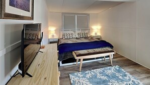 A bedroom with a bed, bedside tables, a TV, and a rug. - Mountains to Sea by Topsail Realty (Holly Ridge)