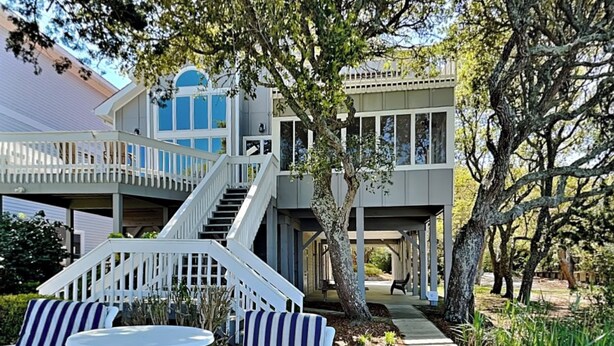 A two-story house with a covered porch, a staircase, and outdoor seating. - The Pack House by Topsail Realty (Holly Ridge)