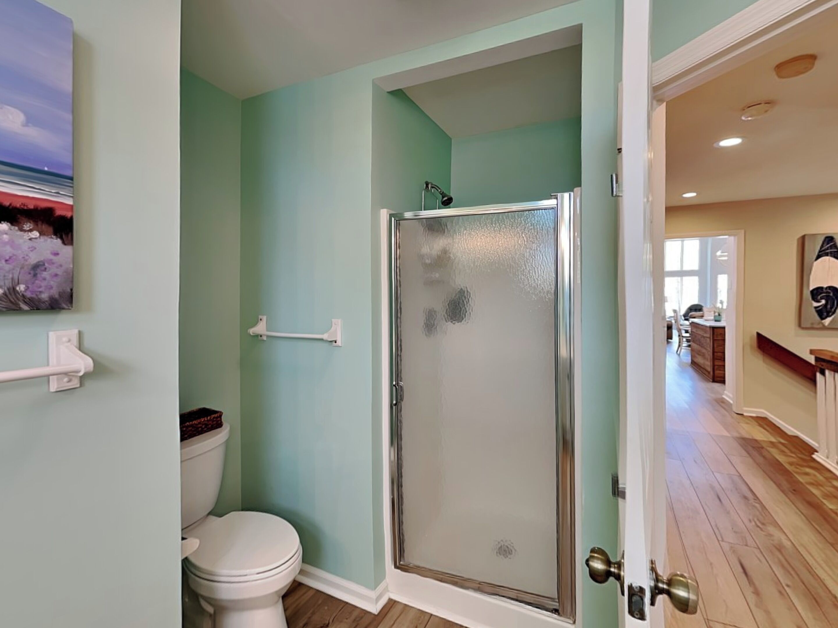 A bathroom with a glass shower door, a toilet, and a handrail.