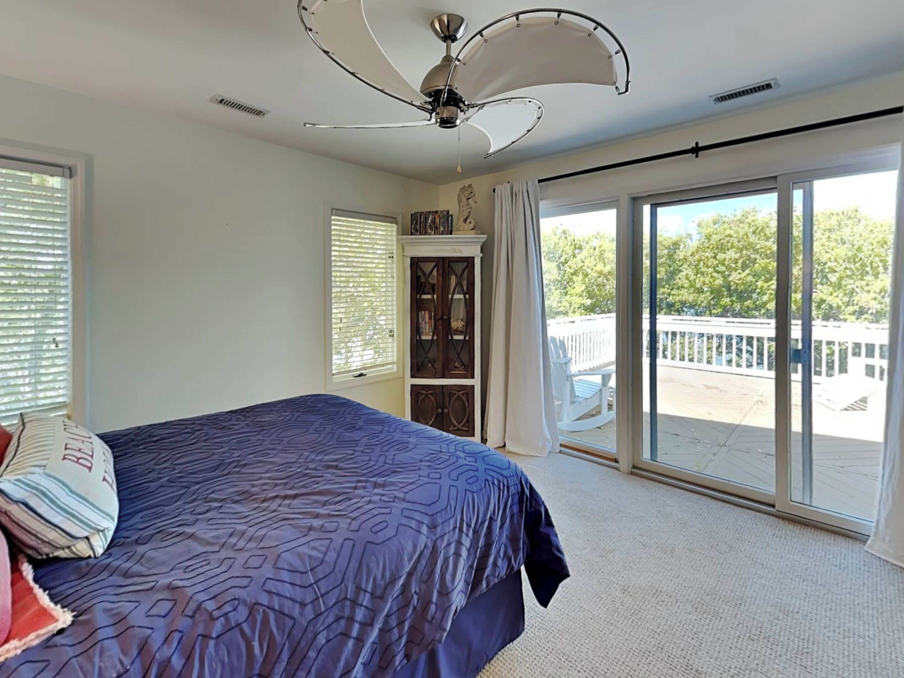 A bedroom with a bed, a ceiling fan, a large window, and a sliding glass door leading to a balcony.