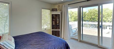 A bedroom with a bed, a ceiling fan, a large window, and a sliding glass door leading to a balcony.