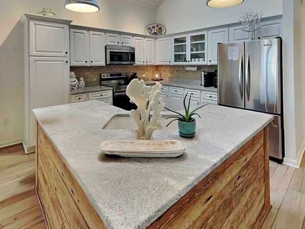 A kitchen with white cabinets, a stainless steel refrigerator, a microwave, and a wooden island with a decorative plant. - The Pack House by Topsail Realty (Holly Ridge)