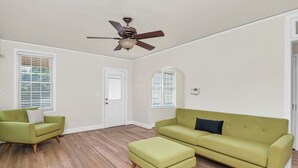 A spacious living room with a green sofa, a matching ottoman, and a ceiling fan. - Comfy West Columbia Get-Away (West Columbia)