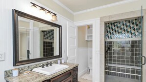 A bathroom with a large mirror, granite countertop, dark wooden cabinets, a white sink, and a glass-enclosed shower with patterned tiles. - Comfy West Columbia Get-Away (West Columbia)
