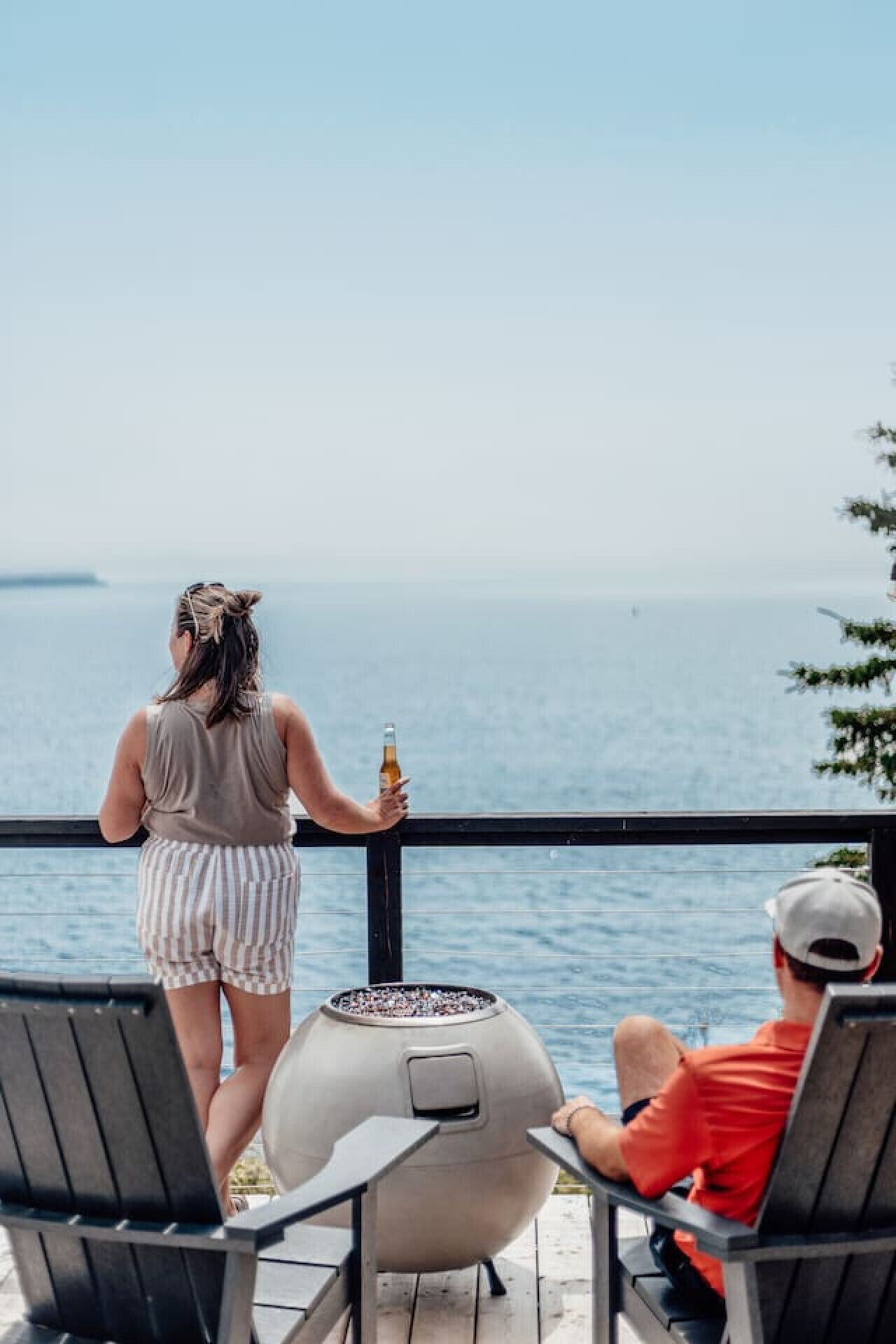 A person holding a bottle on a deck with a view of the sea.