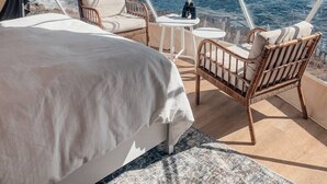Une chambre avec un grand lit, une chaise en osier, une petite table et une vue sur la mer.