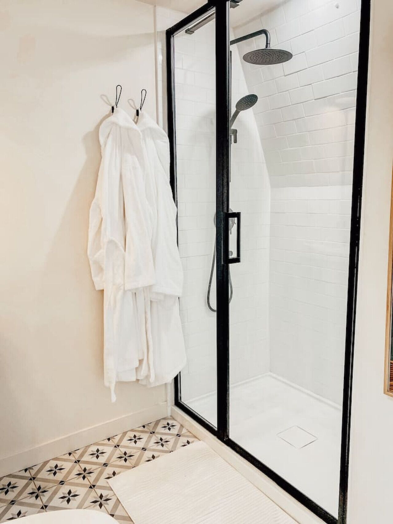 A modern bathroom with a glass-enclosed shower, white tiled walls, and a patterned floor.