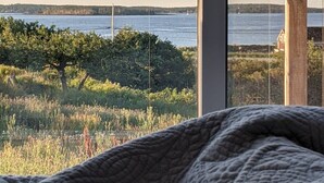 Een bed met uitzicht op een wateroppervlak en een verre kustlijn.
