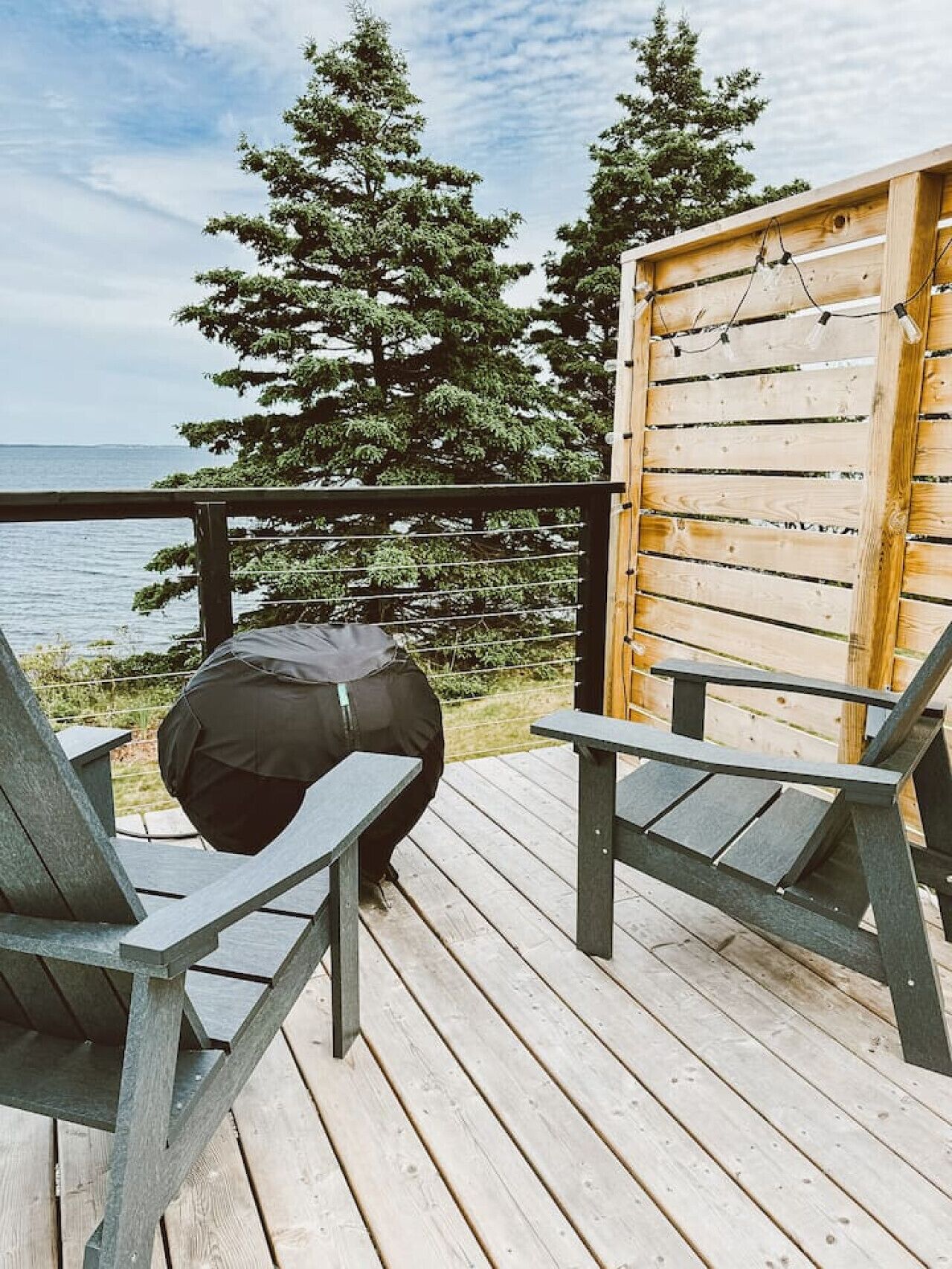 A wooden deck with two chairs and a bench, overlooking a body of water and trees.
