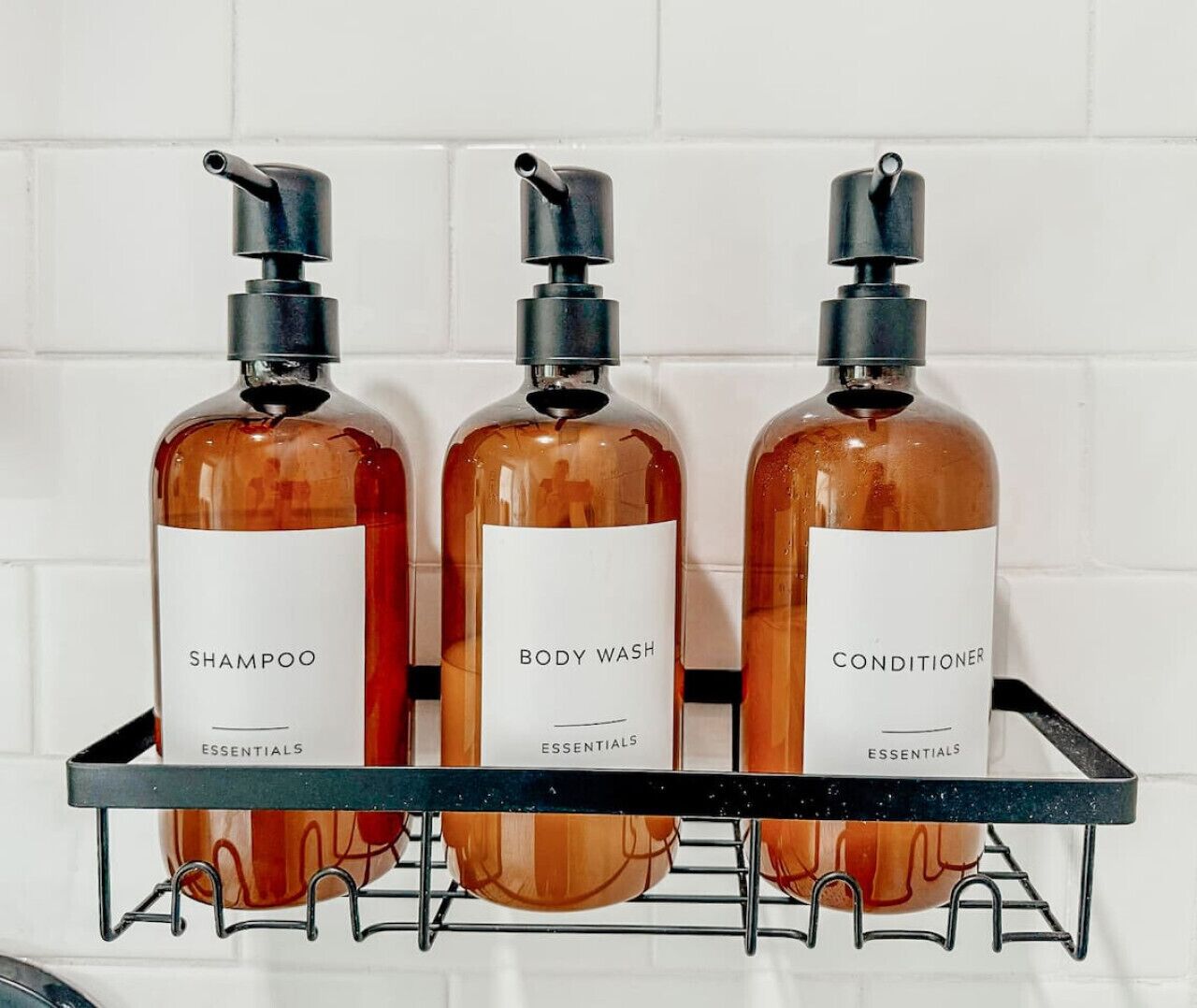 Drie flessen shampoo, douchegel en conditioner op een rek.
