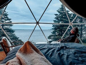 A tent with a view of the sea and trees.