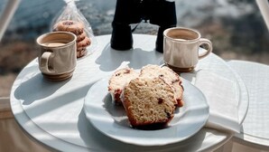 A table with a plate of scones, two cups of tea, and binoculars, set against a scenic view. - Luxury Coastal Dome - Private Hot Tub, Oceanfront Deck, Firepit & Parking (LaHave)