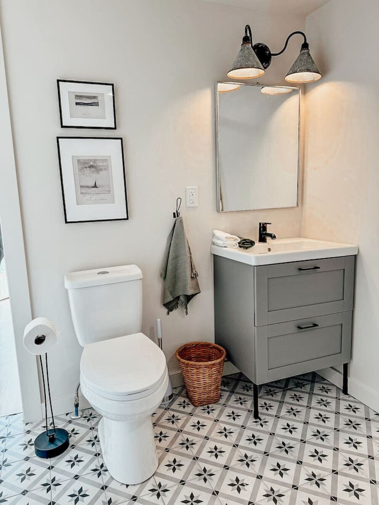Une salle de bain avec des toilettes, un lavabo avec un miroir et deux tableaux encadrés au mur.