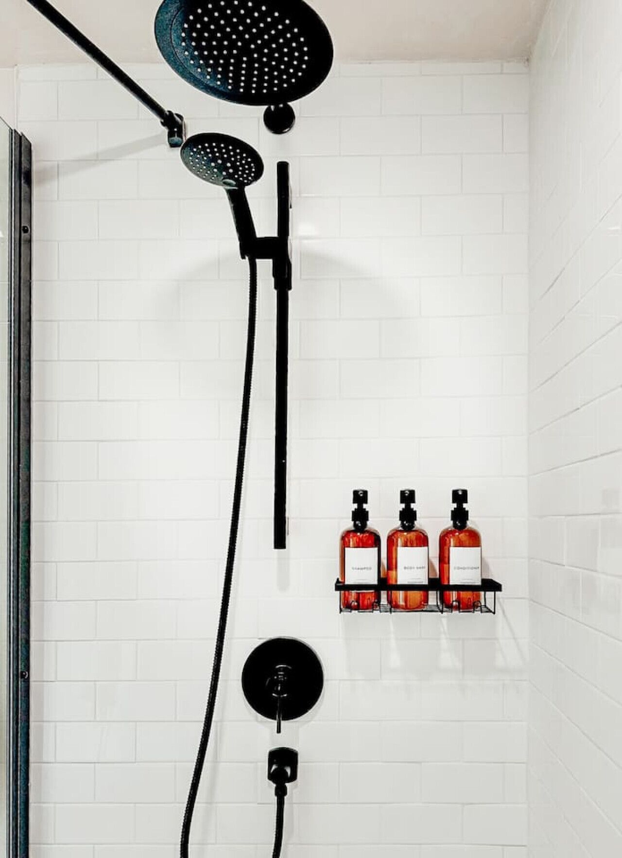 Ein Duschbereich mit Regendusche, Handdusche und Massagebrause. Auf einem Regal befinden sich drei Flaschen Shampoo und Conditioner.
