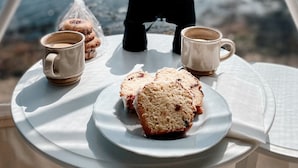 Ein Tisch mit einem Teller voller Muffins, zwei Tassen und Ferngläsern auf einem Balkon mit Blick auf ein Gewässer.