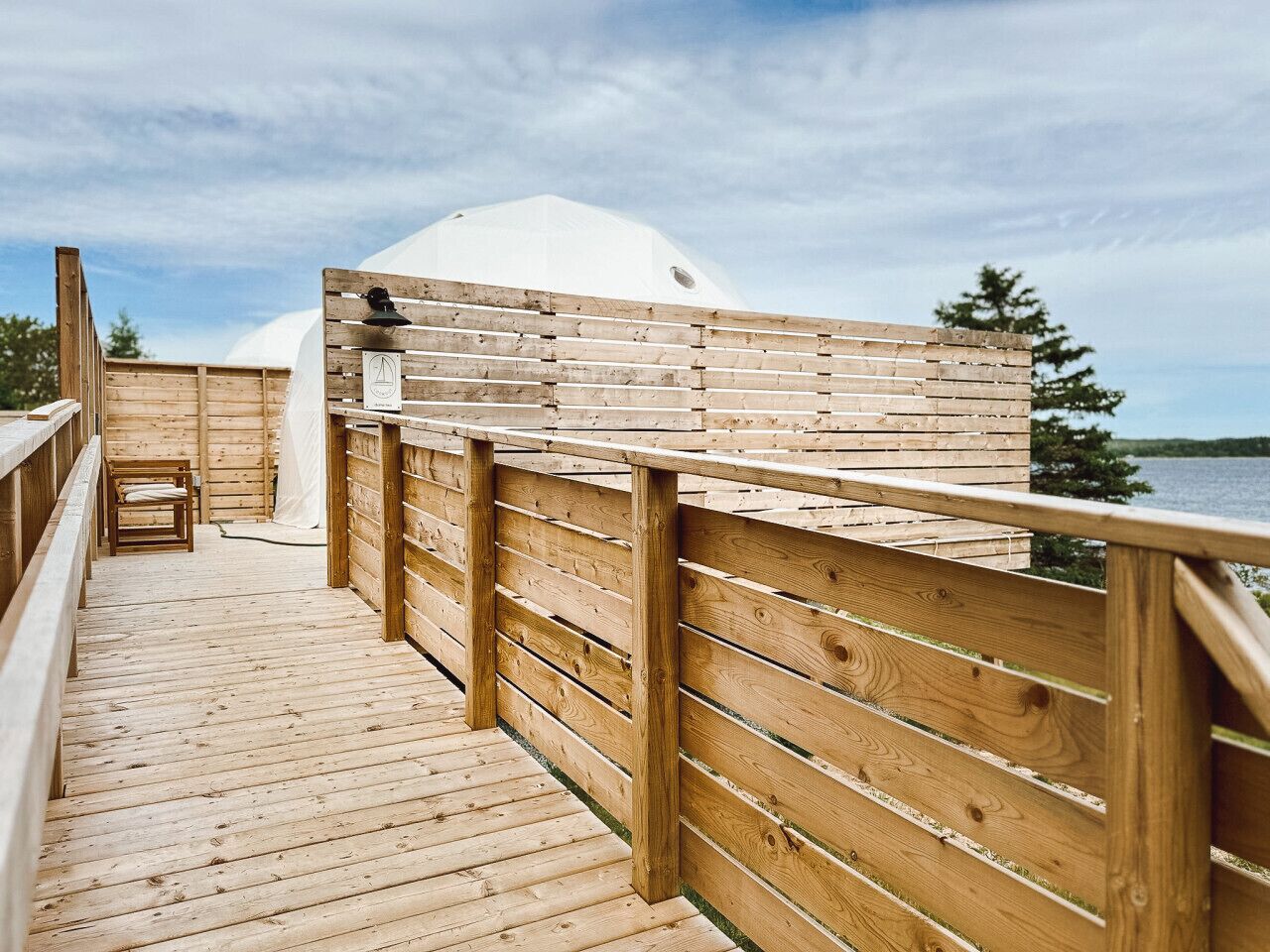 A wooden deck leading to a white dome structure with a view of the water.