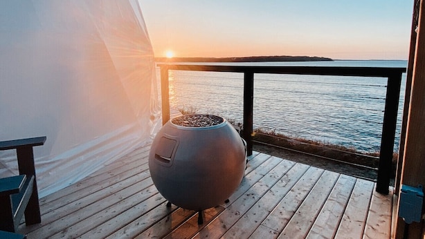 Eine Holzterrasse mit großem Kochherd und einer Bank, mit Blick auf ein Gewässer bei Sonnenuntergang.