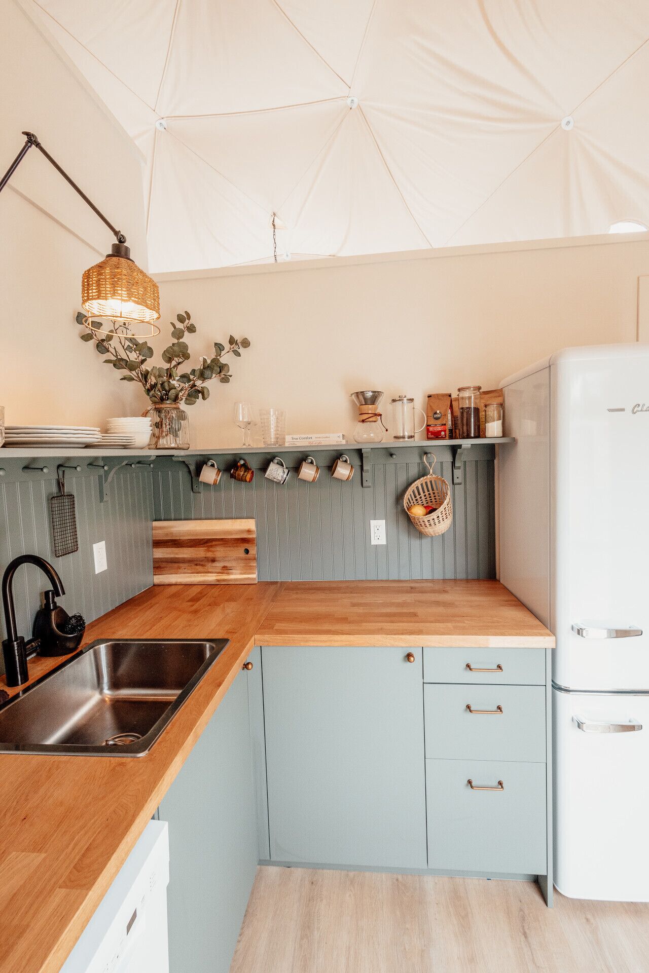 A kitchen with a wooden countertop, a sink, a hanging light fixture, and a refrigerator.