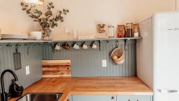 A kitchen with a wooden countertop, a sink, a hanging light fixture, and a refrigerator.