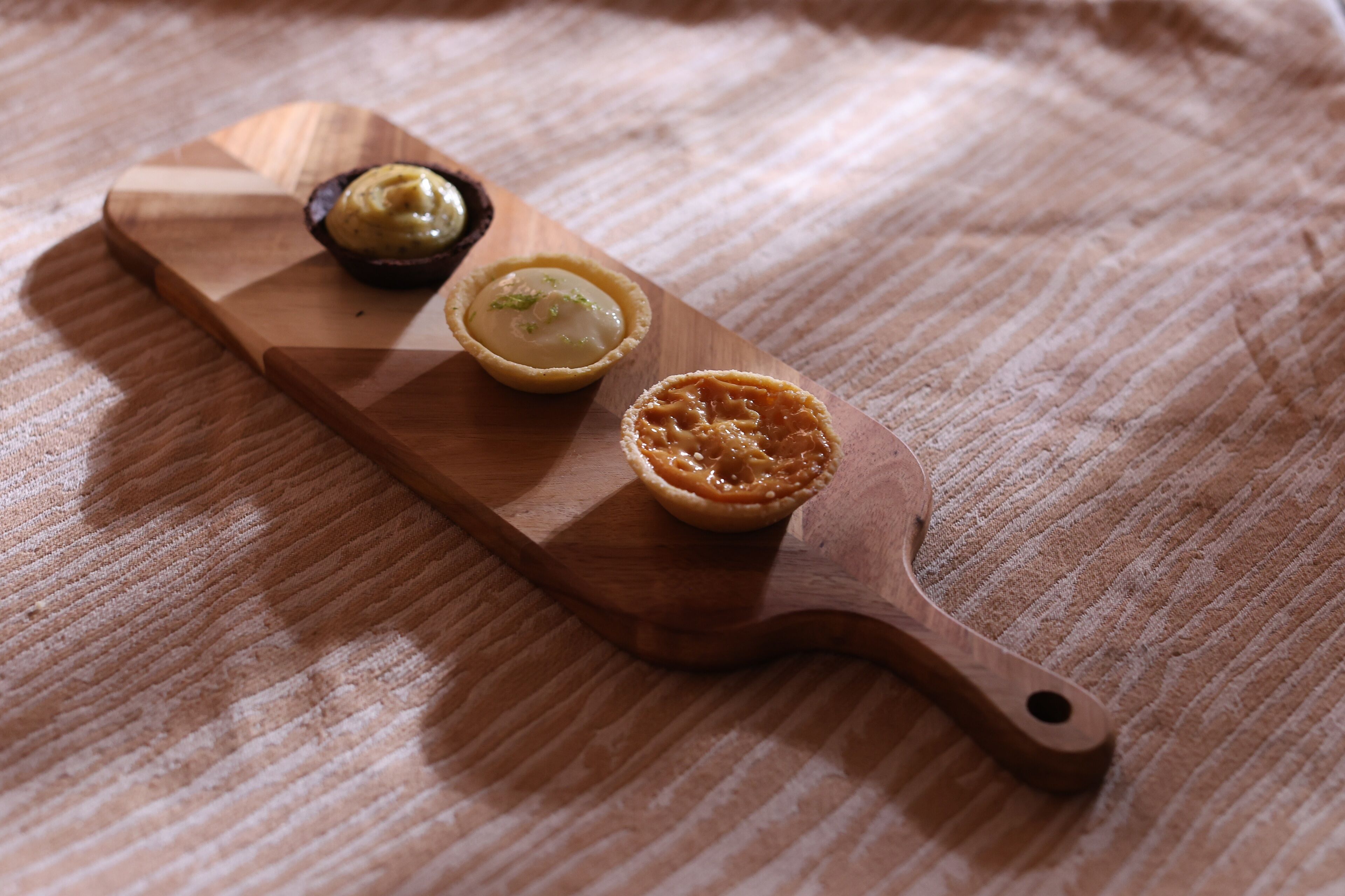 A wooden board with three pastries on a textured fabric surface.