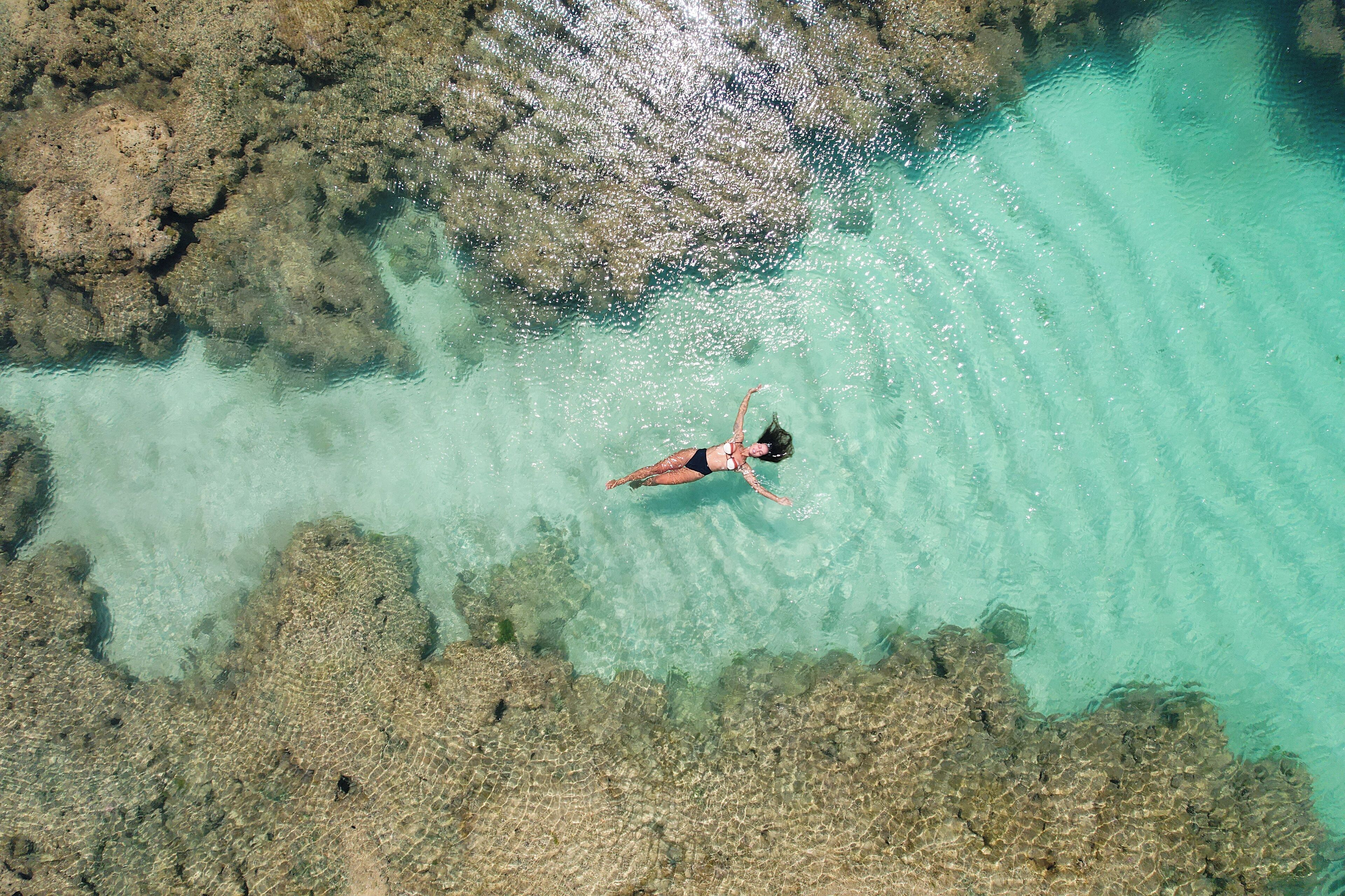 A person swimming in clear turquoise water with rocky formations.