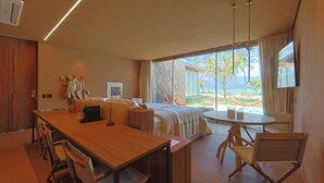 Camera d'albergo moderna con tavolo da pranzo in legno, un letto con una grande finestra e un balcone con vista sulle palme.