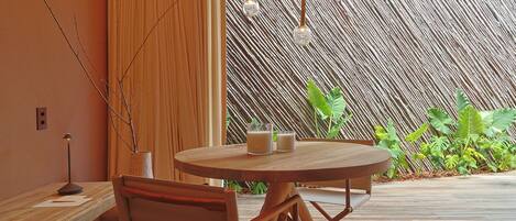 A round wooden table with two glasses of a white beverage, a chair, a lamp, and a decorative hanging light fixture.