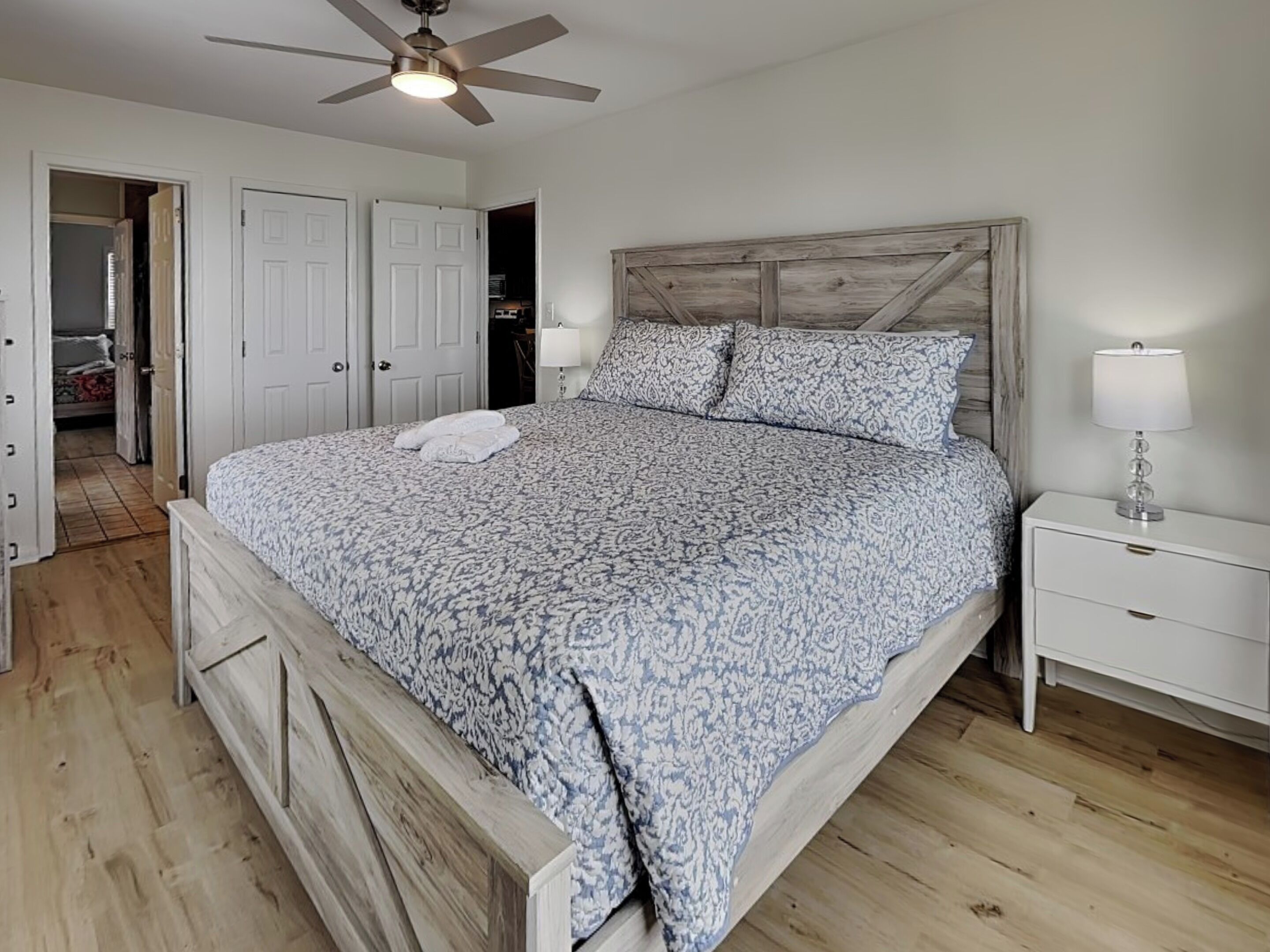 A bedroom with a wooden headboard, a bed with patterned bedding, a nightstand with a lamp, and a ceiling fan.