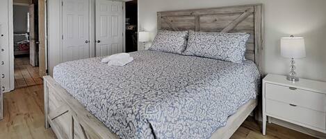 A bedroom with a wooden headboard, a bed with patterned bedding, a nightstand with a lamp, and a ceiling fan.