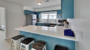 A modern kitchen with a large island, bar stools, and blue cabinetry. - Seaside Serenity by Carolina Retreats (Carolina Beach)