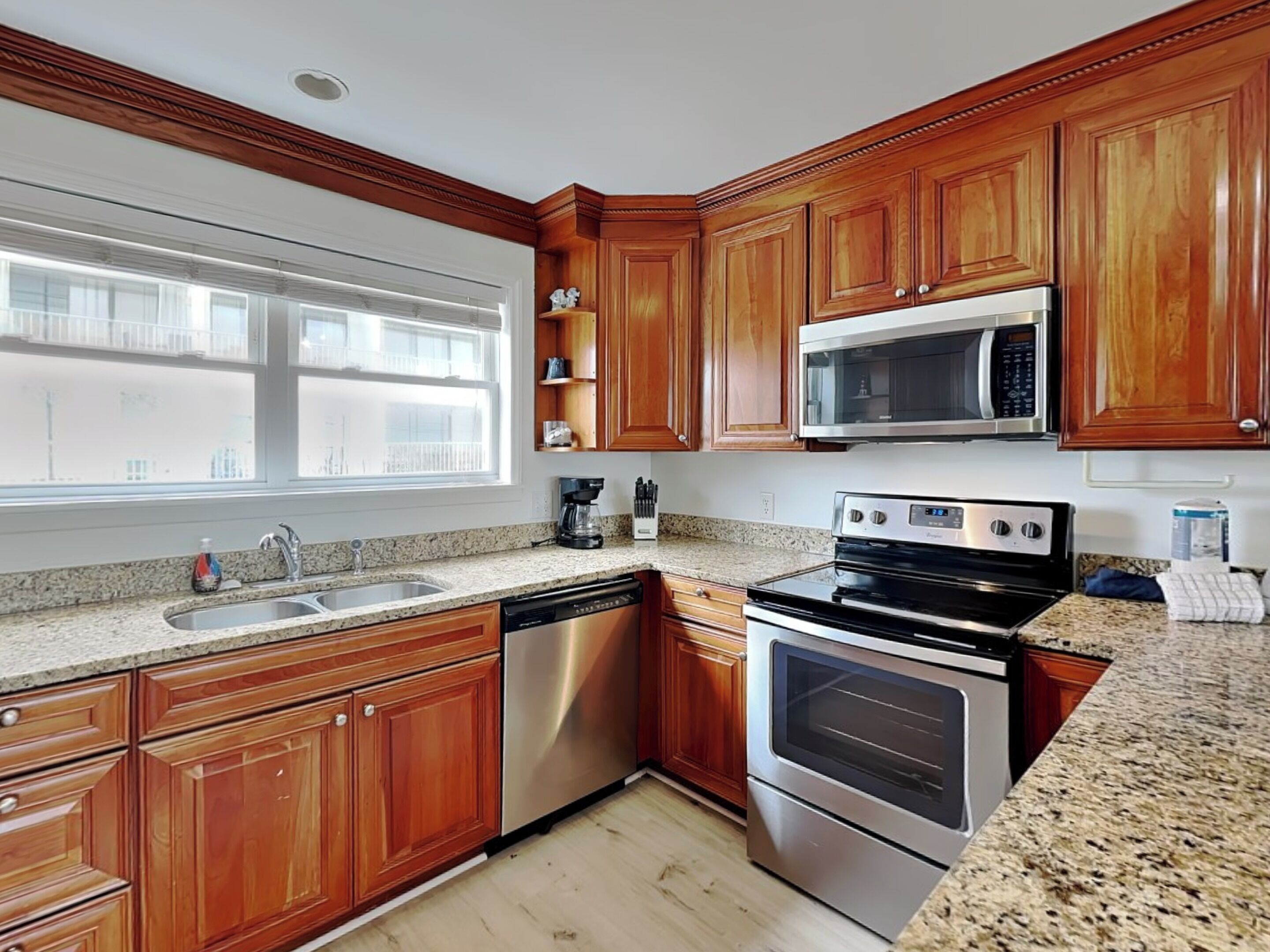 A kitchen with wooden cabinets, stainless steel appliances, granite countertops, and a window with a view.