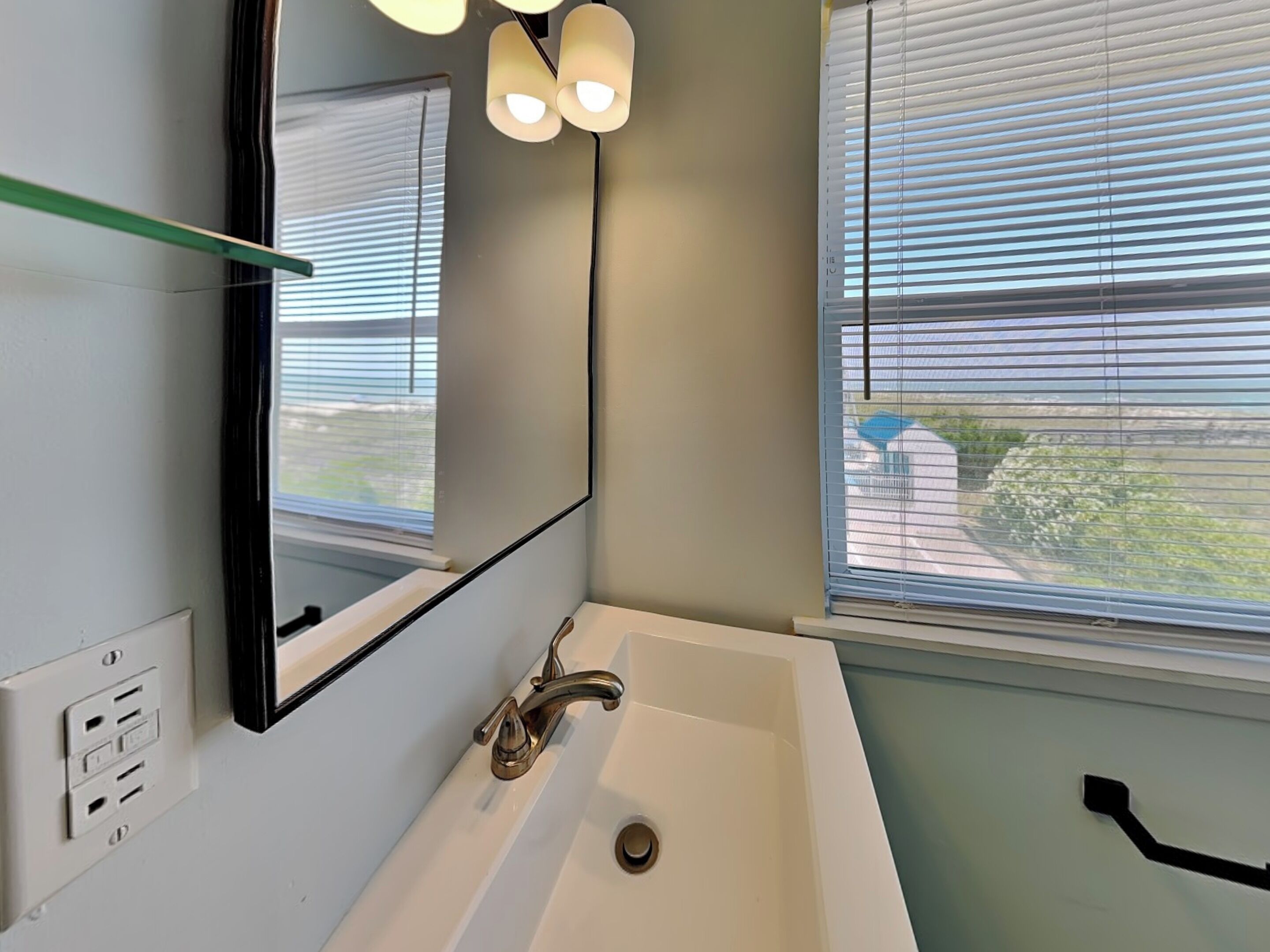 A bathroom with a white sink, a mirror, and a window with blinds.