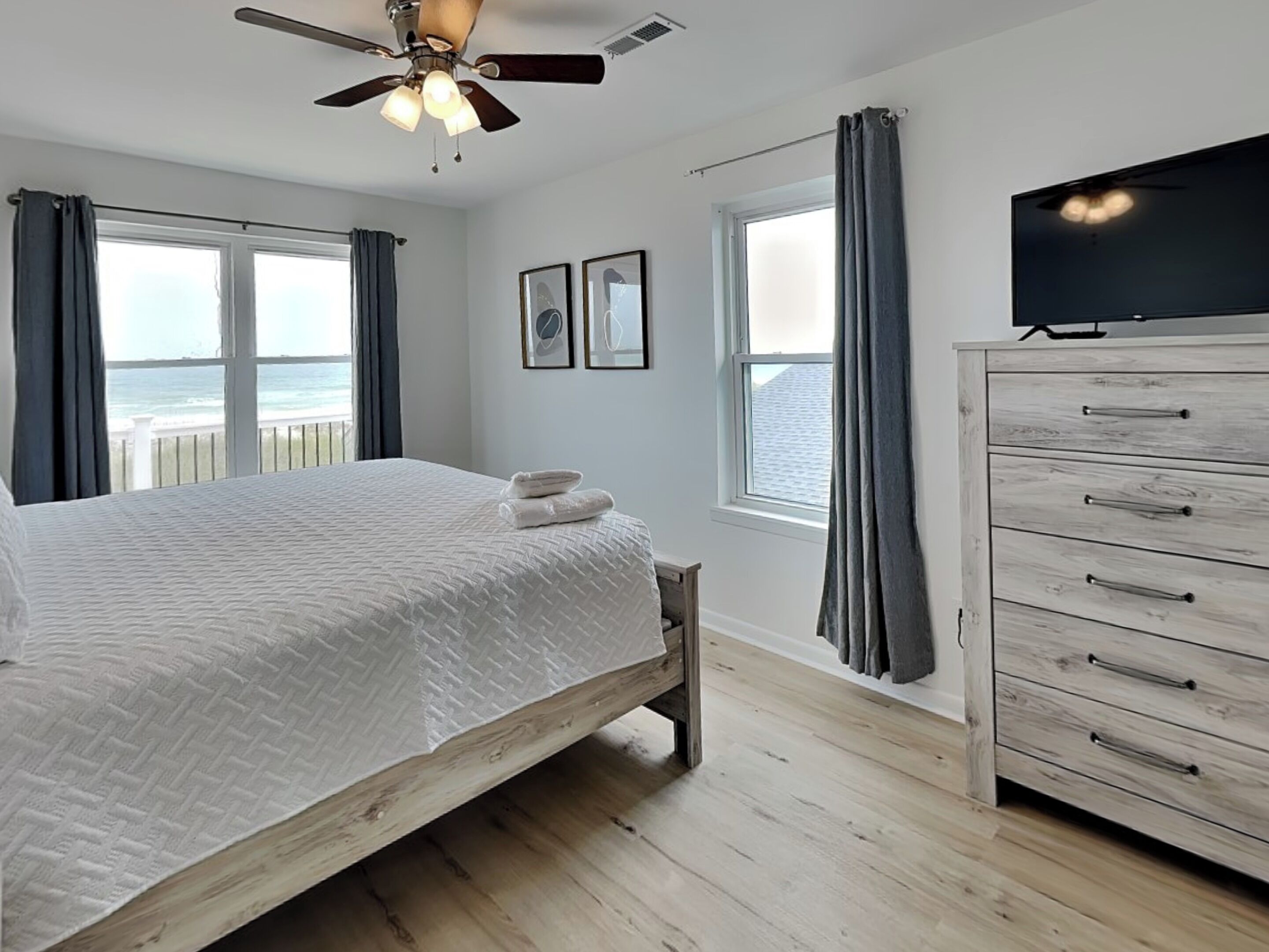A bedroom with a bed, a wooden dresser, a ceiling fan, and a TV.