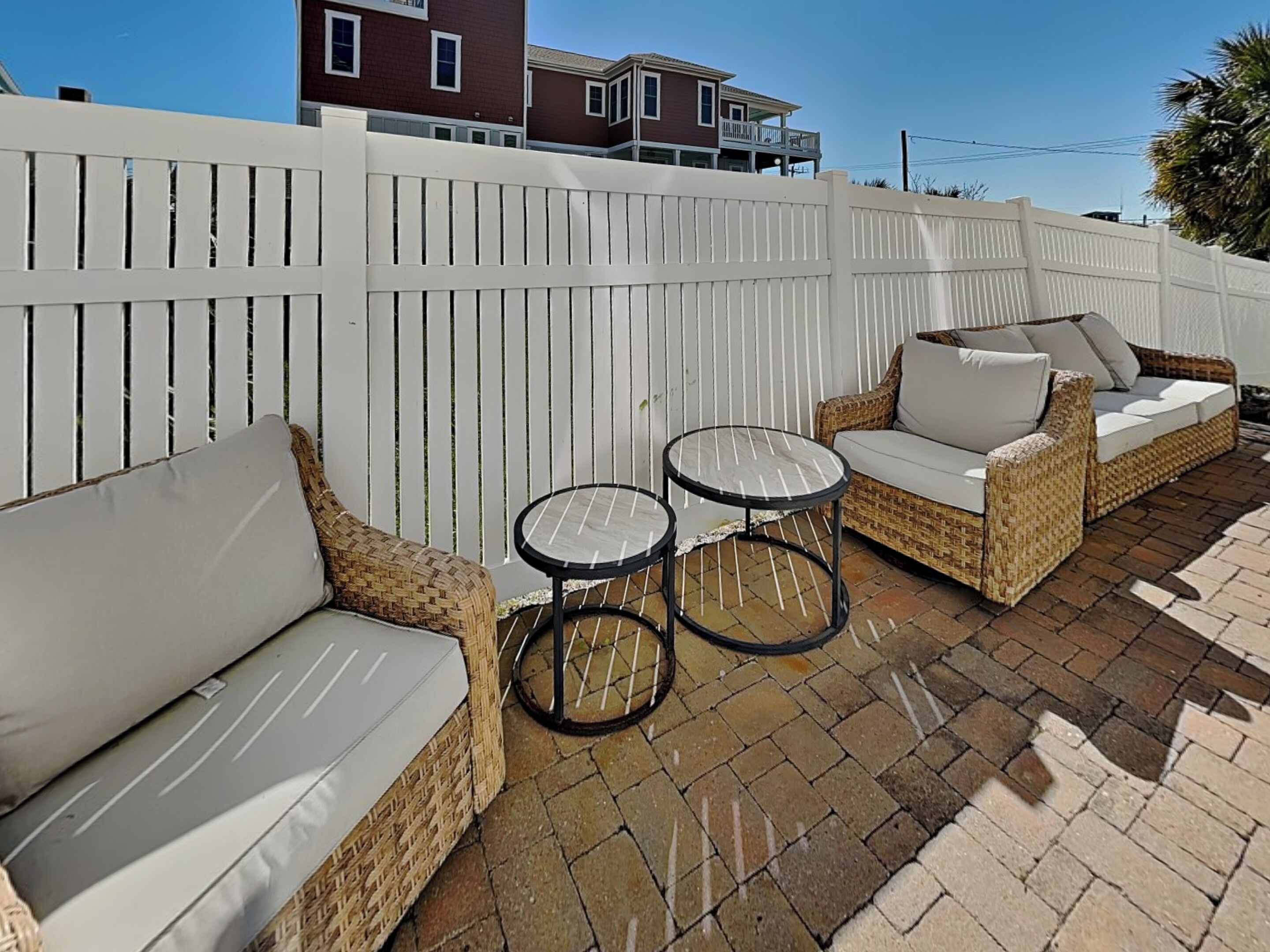 An outdoor patio with wicker furniture, two round tables, and a white fence.