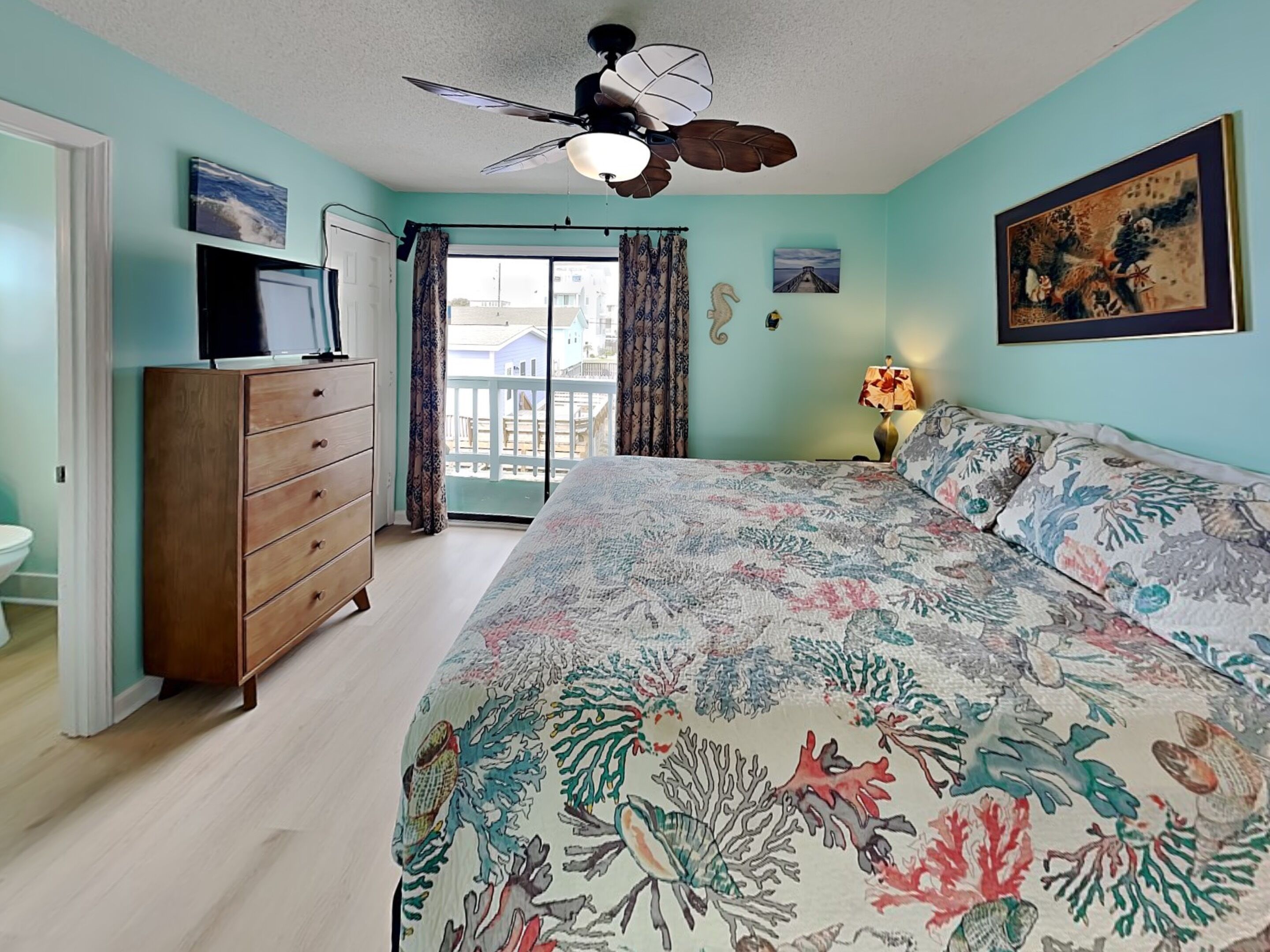 A bedroom with a bed, dresser, ceiling fan, and a view through a window.