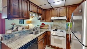A kitchen with wooden cabinets, a dishwasher, a stove, and a refrigerator. - The Sandcastle @ Tiki by Carolina Retreats (Carolina Beach)