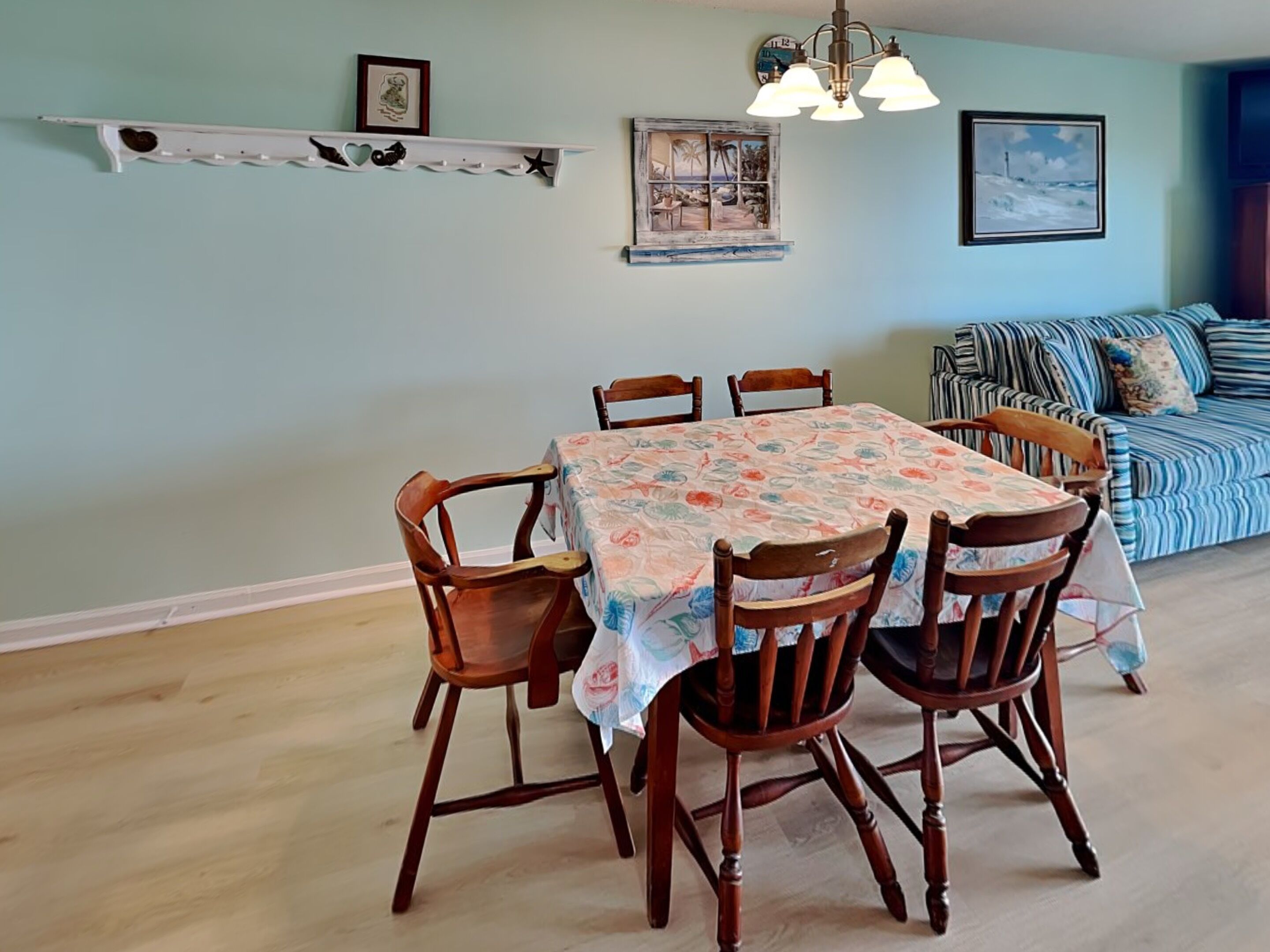 A dining area with a table and chairs, a sofa, a shelf with decorative items, and a wall with a clock and a picture.