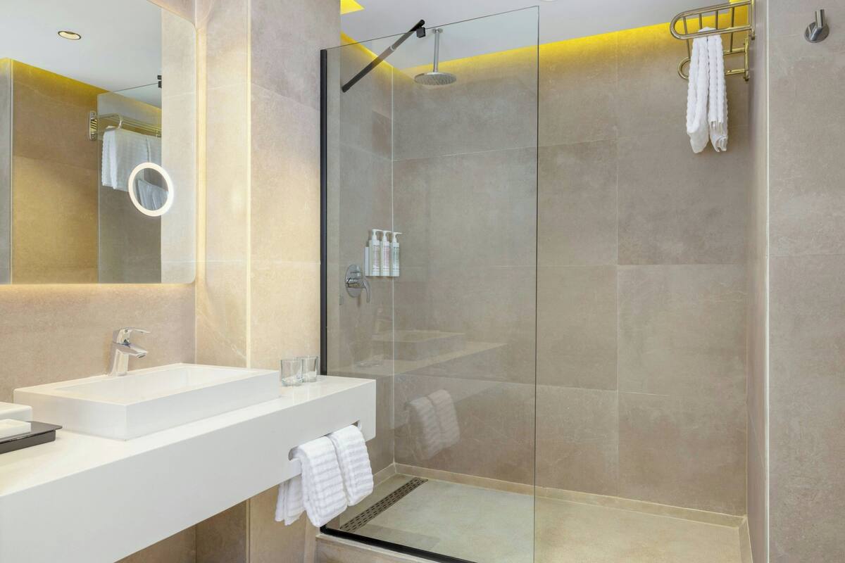 Un baño moderno con ducha de mampara de vidrio, lavamanos blanco y espejo.