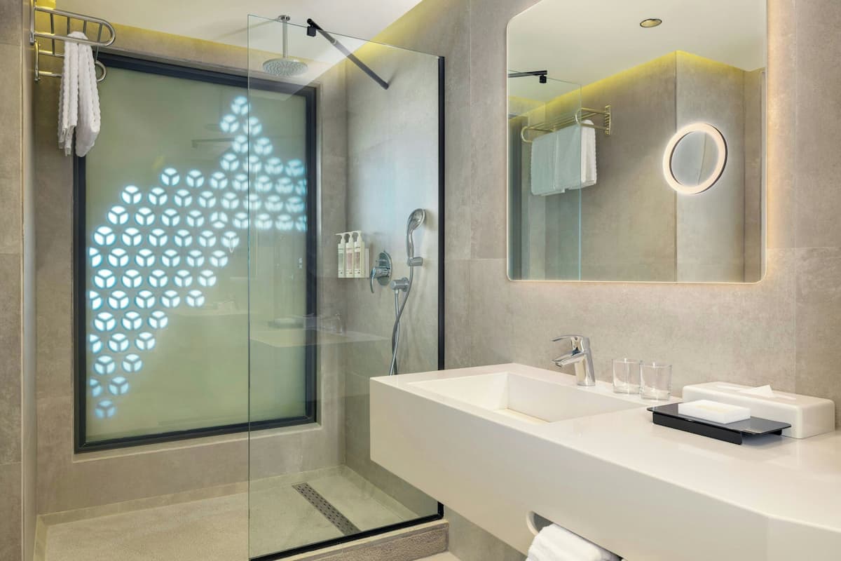 Un baño moderno con cabina de ducha de vidrio, un espejo grande y un mueble de tocador blanco con lavamanos y barra para toallas.