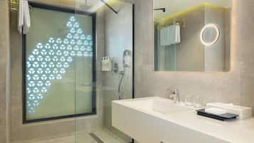 A modern bathroom with a glass shower enclosure, a large mirror, and a white vanity with a sink and towel rack.