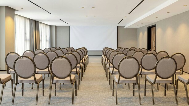 A conference room with rows of chairs facing a blank screen, a large window with curtains, and a modern ceiling with recessed lighting. - Le Méridien Casablanca (Casablanca)