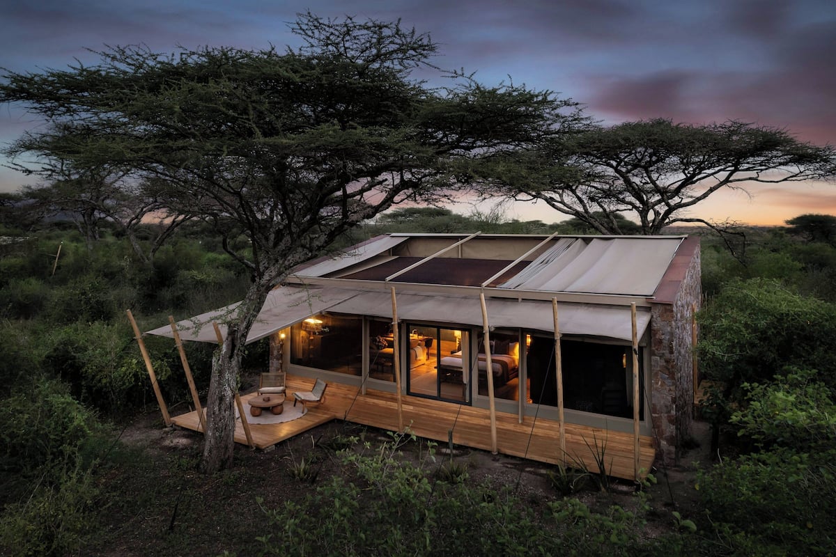 A modern, treehouse-style accommodation with a large glass window, wooden deck, and a cozy interior.
