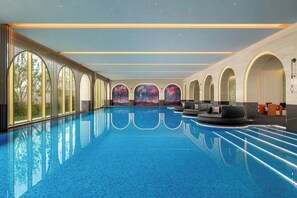 A large indoor swimming pool with clear blue water, surrounded by arched windows and seating areas. - Renaissance Korla Hotel (Korla)