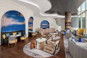 A modern lounge area with leather sofas, round tables, and a large abstract mural on the wall.