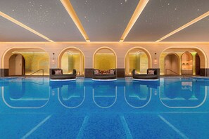 A large indoor swimming pool with clear blue water, surrounded by arched doorways and a starry ceiling.