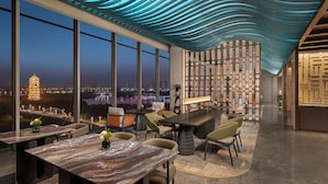A modern dining area with a view of a cityscape, including a bridge and a pagoda. - Renaissance Korla Hotel (Korla)